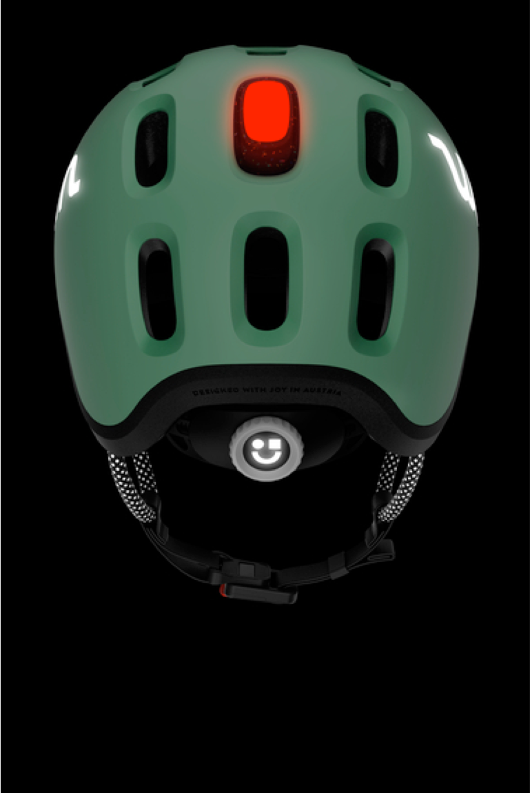 The green READY Kids' Helmet with clipped-in red rear helmet light and reflective details, viewed from behind in the dark